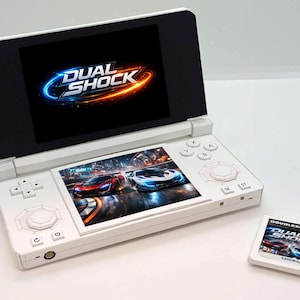 May include: A white handheld gaming console with two screens, displaying the game "Dual Shock." The bottom screen shows race cars. A game cartridge with the same title is next to the console.