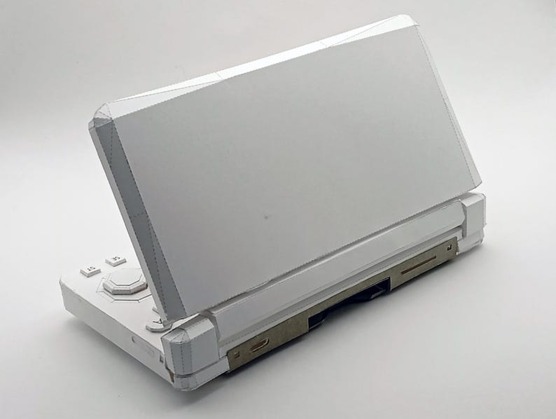 May include: A white handheld gaming console with a hinged design. The console is open, revealing the screen and control buttons. The device has a sleek, modern aesthetic with a minimalist design.