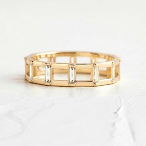 May include: A gold band ring with a geometric design featuring baguette-cut diamonds set in a cage-like pattern.