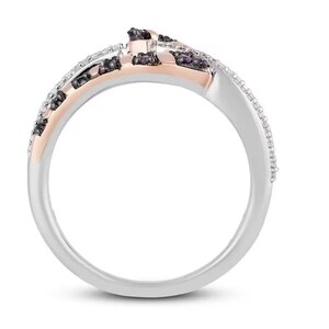 May include: A silver and rose gold ring with black and white diamonds. The ring has a unique design with the diamonds set in a twisted pattern.