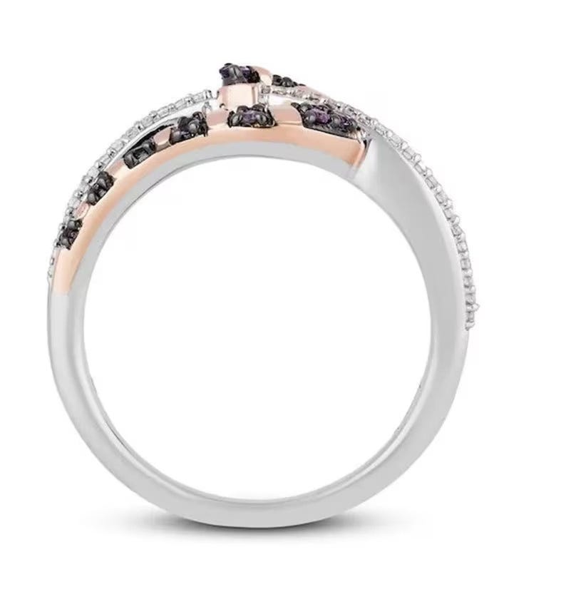 May include: A silver and rose gold ring with black and white diamonds. The ring has a unique design with the diamonds set in a twisted pattern.