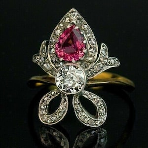 May include: A vintage ring with a pear-shaped pink gemstone surrounded by smaller diamonds. The ring band is gold and the setting is silver with a floral design.