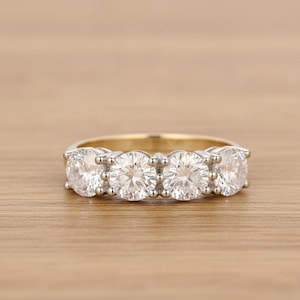 May include: A gold and silver ring with four large, clear gemstones set in a row. The ring is on a wooden surface, and the gemstones sparkle in the light.