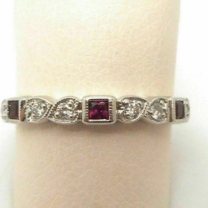 May include: A silver band ring with a red gemstone and small clear gemstones set in a heart shape design.