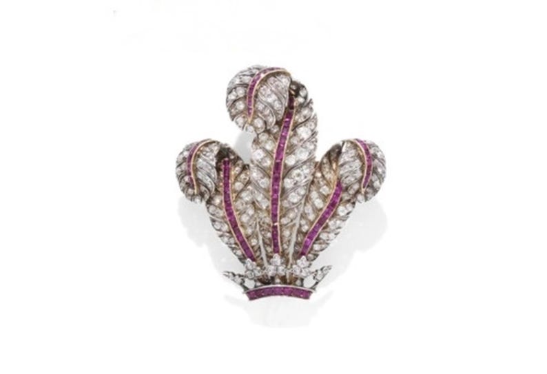 May include: A detailed brooch in the shape of a stylized feather design. The brooch features a silver-colored metal base, adorned with numerous small, clear gemstones and accented with vibrant, deep red gemstones. The design is symmetrical and elegant.