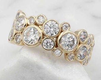 May include: A gold ring featuring multiple round-cut diamonds of varying sizes. The diamonds are set in a cluster design, creating a sparkling, eye-catching effect. The ring is set on a white surface.