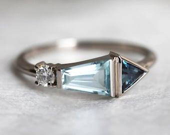 May include: A silver ring with a light blue aquamarine gemstone and a smaller, clear diamond. The aquamarine is set in a triangular shape with a smaller, triangular blue gemstone at the point.