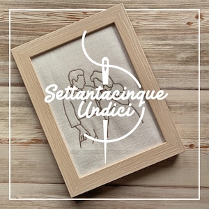Può includere: Un ricamo incorniciato con due figure, con il testo "Settantacinque Undici" in scrittura bianca. L'opera è in una cornice di legno chiaro, su uno sfondo di legno.