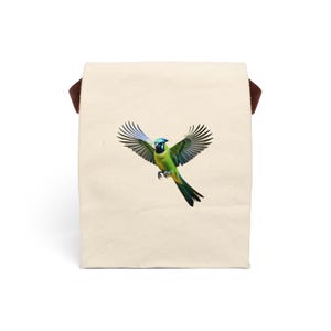 Puede incluir: Una bolsa de lona blanca con correas marrones y un pájaro verde y azul con las alas extendidas en vuelo.