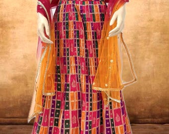 May include: A vibrant, traditional Indian outfit. The ensemble features a red, embroidered crop top and a pleated skirt in a colorful plaid pattern with pink, orange, green, and purple hues. A sheer orange scarf with gold trim completes the look.