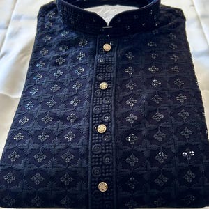 May include: A black embroidered kurta with a stand-up collar and gold buttons. The kurta has a delicate floral pattern and is made of a lightweight fabric.