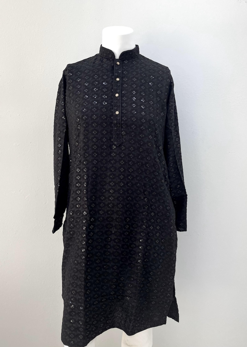 May include: A black long-sleeved shirt with a button-up collar and a geometric pattern. The shirt has a relaxed fit and a slightly longer length.