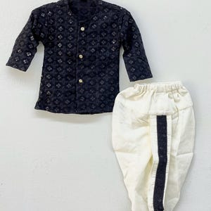May include: A black and white patterned kurta and white dhoti pants. The kurta has a button-up front and long sleeves. The dhoti pants have a black trim down the side.