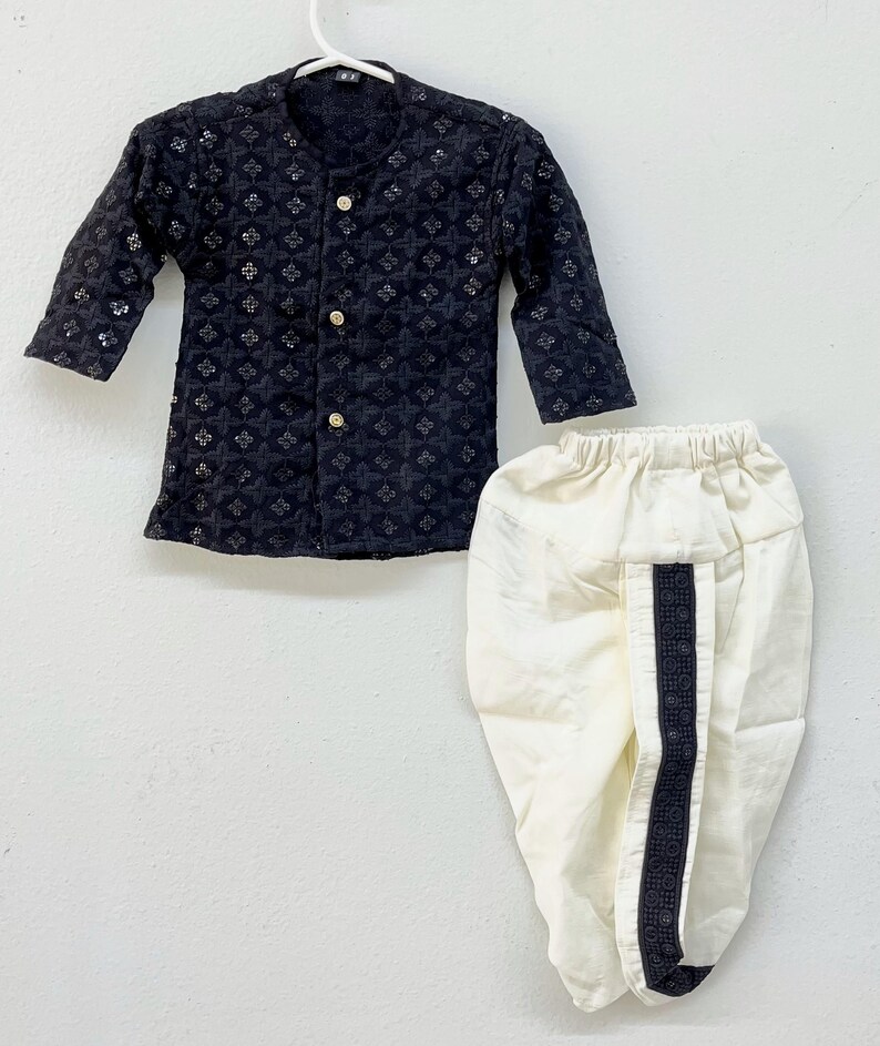 May include: A black and white patterned kurta and white dhoti pants. The kurta has a button-up front and long sleeves. The dhoti pants have a black trim down the side.