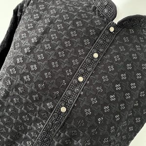 May include: A black embroidered shirt with a mandarin collar and button closure. The shirt has a geometric pattern and is made of a lightweight fabric.