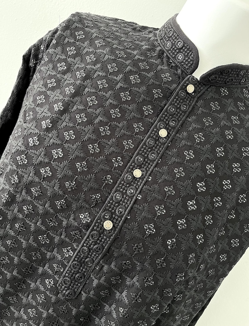 May include: A black embroidered shirt with a mandarin collar and button closure. The shirt has a geometric pattern and is made of a lightweight fabric.