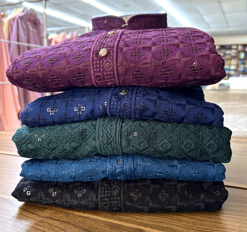 May include: A stack of five embroidered shirts in different colors, including purple, blue, green, and black. The shirts have a geometric pattern and are folded neatly.