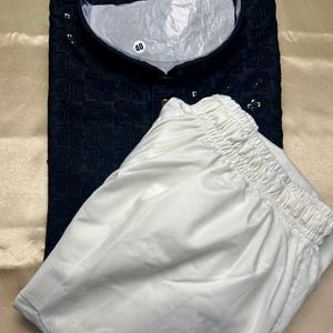 May include: A black kurta with white embroidery and a white drawstring pajama. The kurta has a mandarin collar and a button closure. The size tag reads "40".