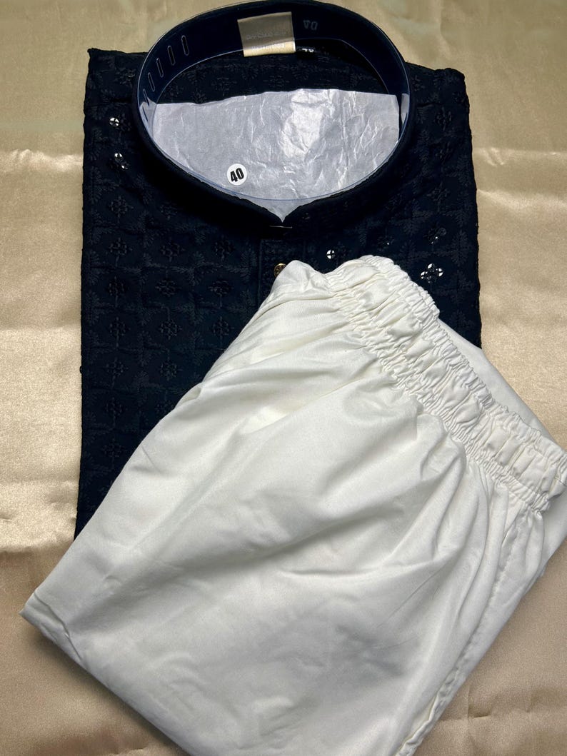 May include: A black kurta with white embroidery and a white drawstring pajama. The kurta has a mandarin collar and a button closure. The size tag reads "40".