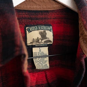 May include: Red and black plaid flannel shirt with a brown corduroy collar. The shirt features a label with the text "FIELD & STREAM SINCE 1871". The shirt is a size large.