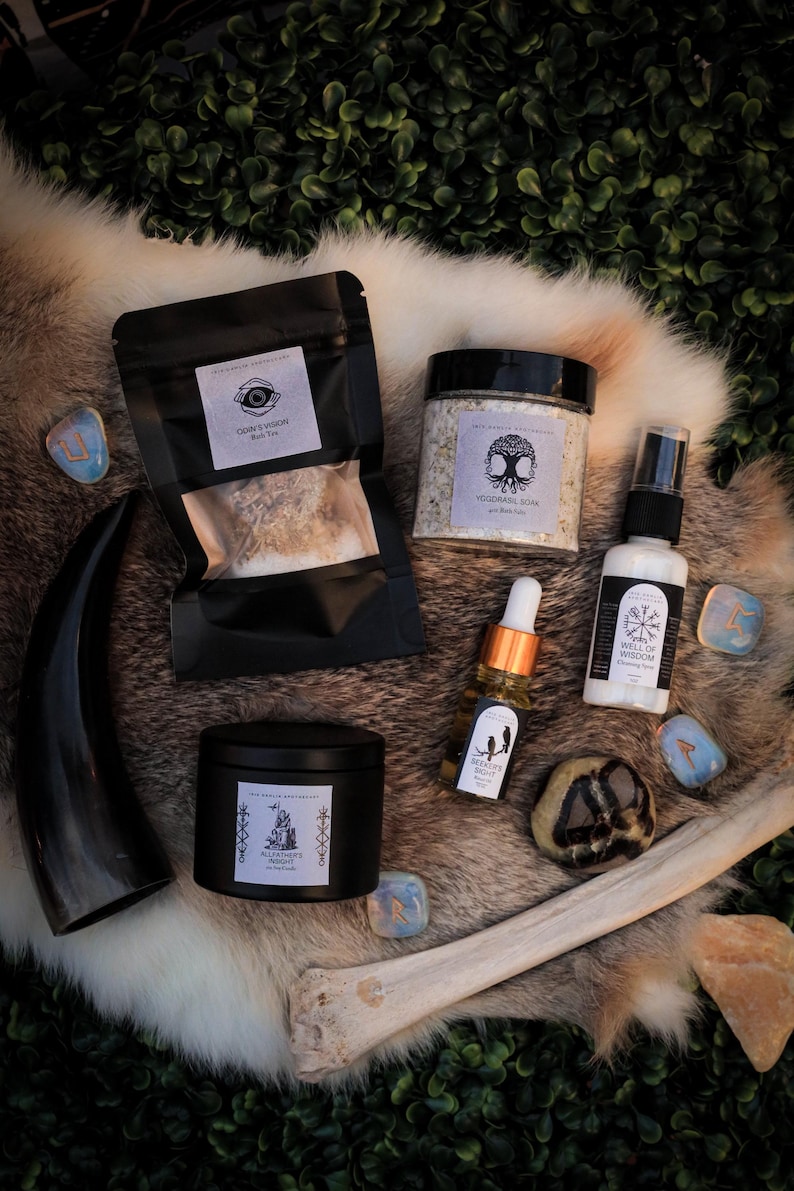 Puede incluir: Un surtido de productos espirituales y de bienestar, que incluyen una vela negra, una bolsa negra de t&eacute;, un tarro de sales de ba&ntilde;o y una botella de aceite. Los art&iacute;culos est&aacute;n dispuestos sobre una superficie similar a la piel con runas y un hueso.