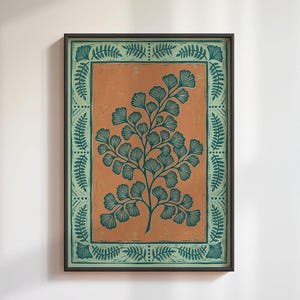 Puede incluir: Lámina botánica enmarcada con una planta similar a un helecho de color verde azulado sobre un fondo naranja. La obra de arte está encerrada dentro de un borde verde azulado con un patrón de hojas repetido, todo en un marco negro. Una pieza decorativa para el hogar.