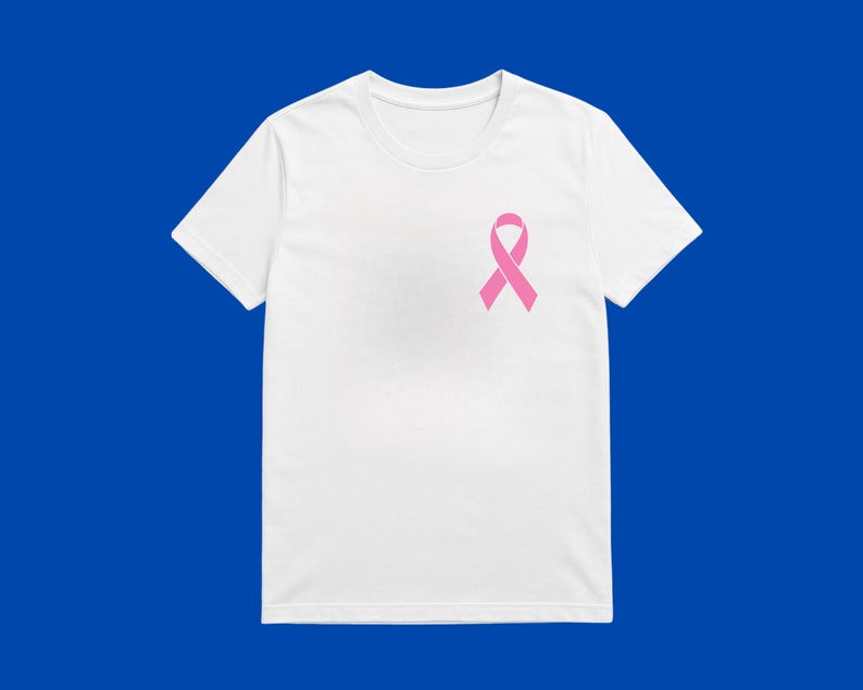 May include: A white t-shirt featuring a pink awareness ribbon on the left breast. The short-sleeved top is made of a soft material and is set against a blue background. The ribbon is a symbol of support.