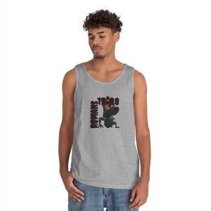 May include: A gray tank top with a graphic design featuring the text "ROMANS 10:20" in dark red. The graphic includes a stylized illustration of a figure. The tank top is sleeveless.