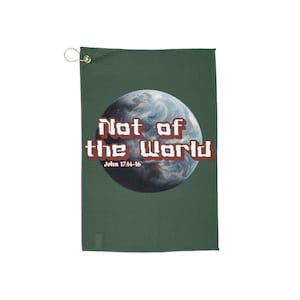 Op de afbeelding: Een donkergroene handdoek met een goudkleurige oogje en een bedrukt ontwerp. Het ontwerp toont een blauwe en witte afbeelding van de aarde met de woorden "Not of the World" in witte en rode letters. De tekst "John 17:14-16" staat eronder.