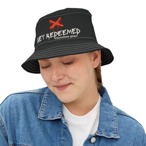 Puede incluir: Sombrero de cubo negro con un gráfico blanco que dice "GET REDEEMED Christian gear" con una X roja sobre la palabra "GET".