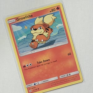 May include: A Growlithe Pokemon card from the Sun & Moon expansion. The card features an illustration of Growlithe, a fire-type Pokemon, with a light brown body, a yellow mane, and a black nose. The card has an HP of 80 and a Take Down attack that does 20 damage to itself. The card is in good condition.
