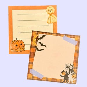 Könnte beinhalten: Zwei quadratische Notizblöcke mit Halloween-Motiven. Einer zeigt einen Kürbis, ein Gespenst und horizontale Linien. Der andere hat einen karierten Rand, eine Mondsichel, Fledermäuse, zwei Katzen in Kostümen und zwei hellviolette Klebestreifen an den Ecken.