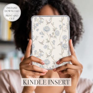 Peut inclure: Un insert Kindle avec un motif floral de fleurs bleues et d'oiseaux sur un fond crème. L'insert est tenu devant une personne. Le texte "INSTAND DOWNLOAD PRINT AND CUT" est dans un cercle en haut à gauche. Le texte "KINDLE INSERT" est en bas.