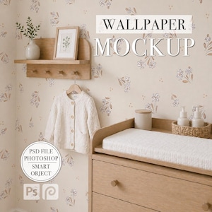 Può includere: Mockup di cameretta con fasciatoio in legno, mensola con stampa incorniciata e cardigan color crema su gruccia in legno. La carta da parati floreale e il testo "WALLPAPER MOCKUP" creano un'atmosfera morbida e invitante.