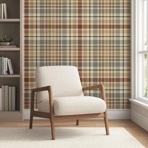 May include: A cream-colored armchair with wooden arms and legs sits on a white rug. The chair is in front of a wall covered in a plaid pattern of brown, beige, green, and black. A bookshelf is visible on the left side of the image.