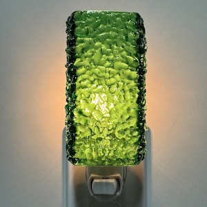 May include: A rectangular night light featuring a textured, translucent green glass cover with a pebbled surface. The glass emits a warm, soft glow from the internal light source, mounted on a white plastic plug-in base with a small toggle switch.