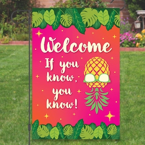 May include: A pink and orange welcome garden flag with a pineapple wearing sunglasses and the text "Welcome If you know, you know!"  The flag has green tropical leaves around the edges.