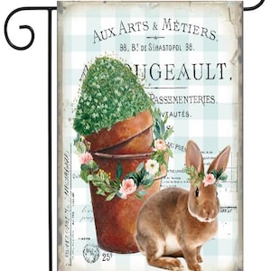 May include: A vintage-style garden flag featuring a brown bunny rabbit wearing a flower crown, sitting in front of a potted plant with a blue and white checkered background. The text on the flag reads "Aux Arts & Métiers. 98, B! de Sébastopol 98.  Dugeault. Passementeries. Vautés."