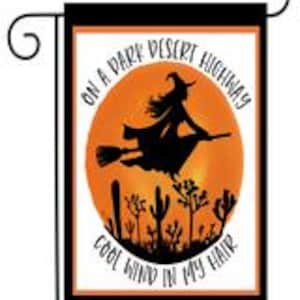 May include: A garden flag with a silhouette of a witch flying on a broomstick against a sunset background with the text "On a dark desert highway, cool wind in my hair".