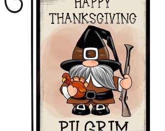 May include: Thanksgiving garden flag featuring a cartoon pilgrim gnome holding a turkey and a rifle. The flag has the words "Happy Thanksgiving Pilgrim" in black text on a beige background, with a black border and a metal hanging loop.
