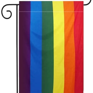 Puede incluir: Una bandera del orgullo arcoíris con los colores morado, azul, verde, amarillo, naranja y rojo. La bandera está unida a un asta de bandera de jardín de metal negro.