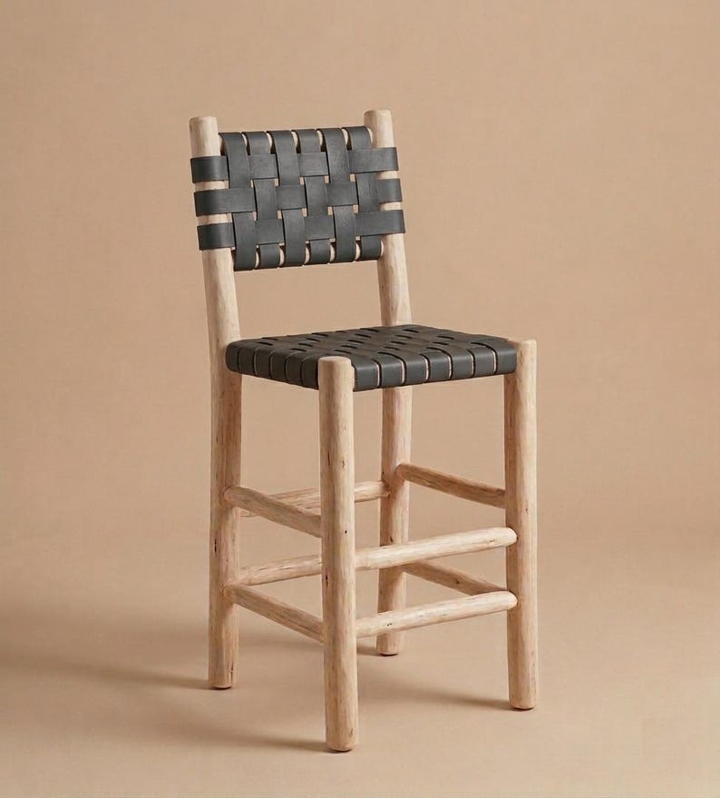 May include: A bar stool featuring a light-colored, natural wood frame with four cylindrical legs and horizontal support rungs. The seat and backrest are constructed from wide, black leather straps woven in a grid pattern across the frame.