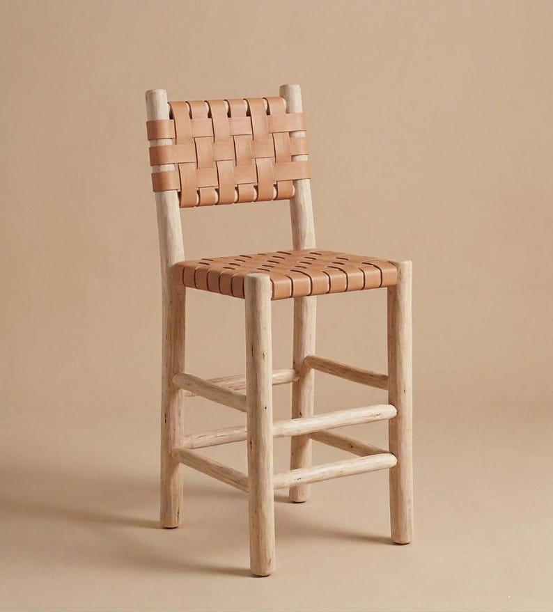 May include: A bar stool featuring a light-colored wooden frame with four cylindrical legs and horizontal support rungs. The seat and backrest are constructed from tan leather strips woven in a grid pattern, providing a structured surface.