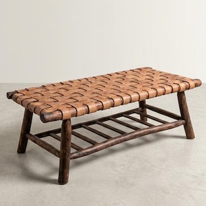 May include: A rectangular coffee table with a woven leather top and a dark brown wooden frame. The table has a lower shelf for storage and is supported by four angled legs. The leather is a light brown color.