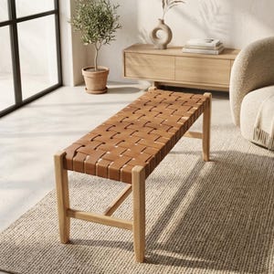 May include: A rectangular bench featuring a seat constructed from wide, tan-coloured woven straps. The frame and four legs are made of light-toned wood, with horizontal support bars connecting the legs on the sides for structural stability.