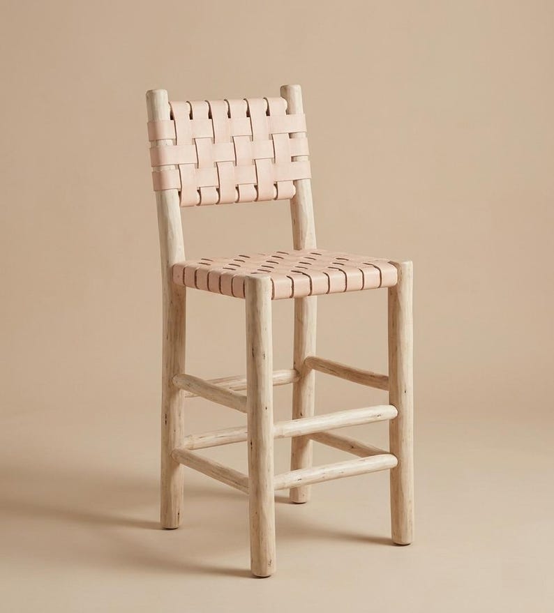 May include: A bar stool featuring a light-colored wooden frame with four cylindrical legs and horizontal support rungs. The seat and backrest are constructed from wide, light beige leather strips woven together in a simple grid pattern.