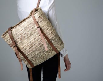 May include: A woven straw backpack with brown leather straps. The backpack is worn by a person, but the person is not visible in the image.