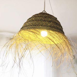 May include: A woven straw pendant light with a fringe of natural fibers. The light is hanging from a ceiling and is illuminated by a light bulb.