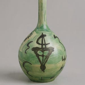Peut inclure: Un vase en céramique vert avec un corps bulbeux et un long col. Le vase présente des motifs noirs abstraits et le texte "BohoHomeDecorMA". C'est un objet décoratif.