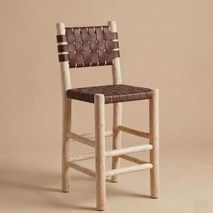 May include: A bar stool featuring a frame constructed from light-colored, natural wood with a visible grain. The seat and backrest are composed of dark brown leather strips woven together in a grid pattern, supported by four legs and horizontal rungs.